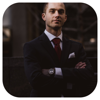 Photographie d'un homme légèrement souriant, en costume noir, cravate rouge et chemise blanche, qui croise les bras. 